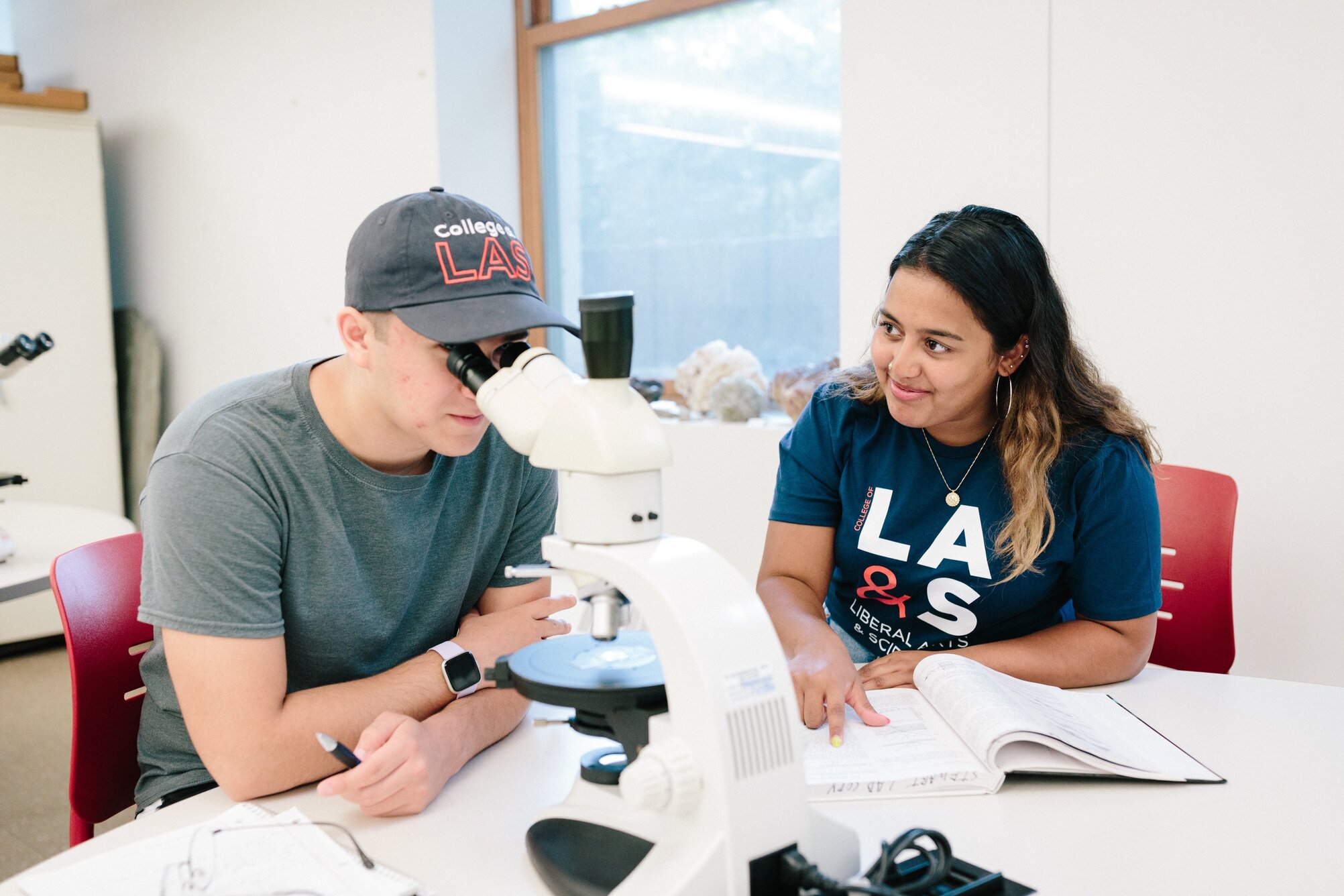 student looking through microscope while another takes notes