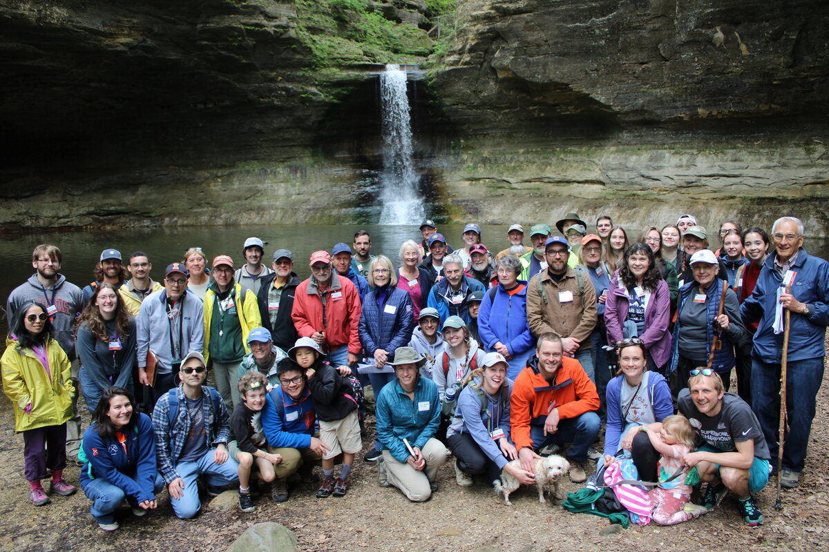 A group of people and a dog posing for a group photo in front of a waterfall.