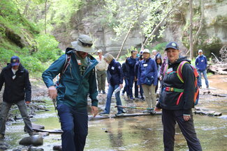 A woman smiles as she helps people cross a creek