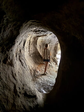 A girl stands in the mouth of a cave while standing out in the dark
