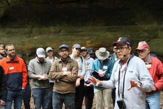 A person lectures a group of people about sandstone