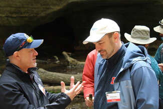 A man wearing a hat tries to convince another man in a hat of something