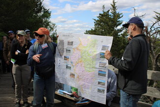 A person points at a map while talking about it as another person helps them hold up the map.