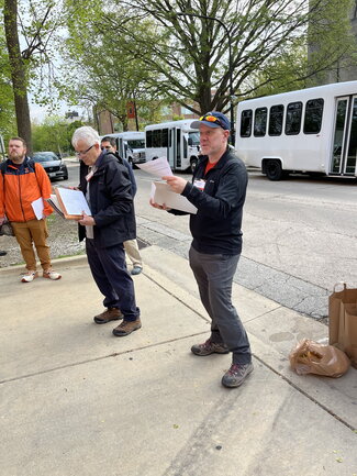 A person talking to a group with two men standing off to the side