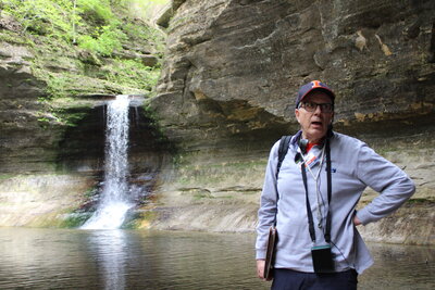 A man standing in front of a waterfall with a hand on his hip.