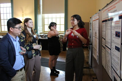 Someone presenting their poster to a pair of listeners.