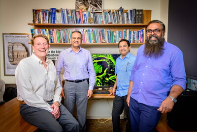 A group of researchers posing for a group photo in someone's office in front of a computer model of their research.