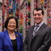 A woman and a man standing in front of a wall of leis.