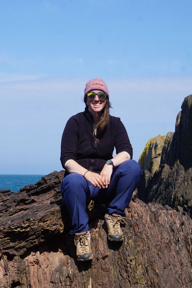 Sarah Austin. A woman sitting on rocks by the sea.
