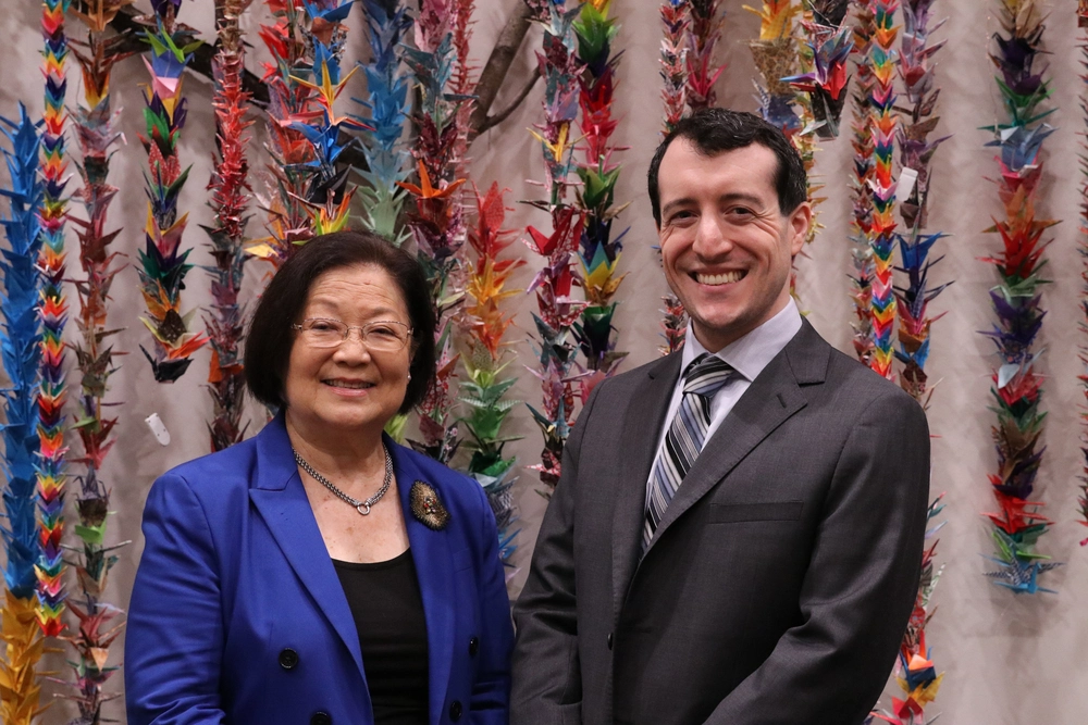 A woman and a man standing in front of a wall of leis.