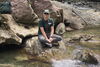 Jenna Shelton. A woman sitting on a rock next to a creek posing for the camera.
